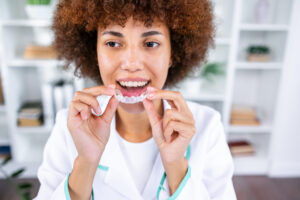Woman smiling while holding a clear aligner tray during dental treatment