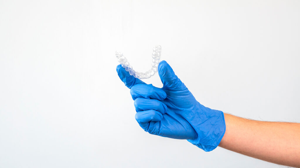 Gloved hand holding a clear dental aligner retainer