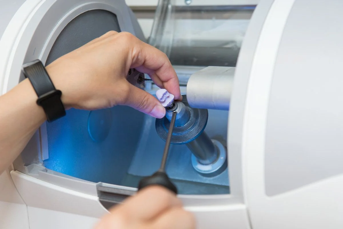 Dental team member setting a workpiece in a CEREC milling machine to manufacture a dental crown